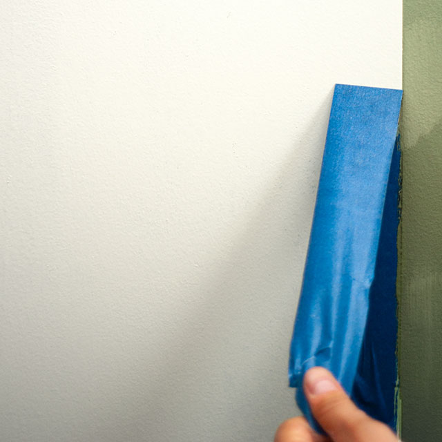 Peeling painter's tape from a white wall.