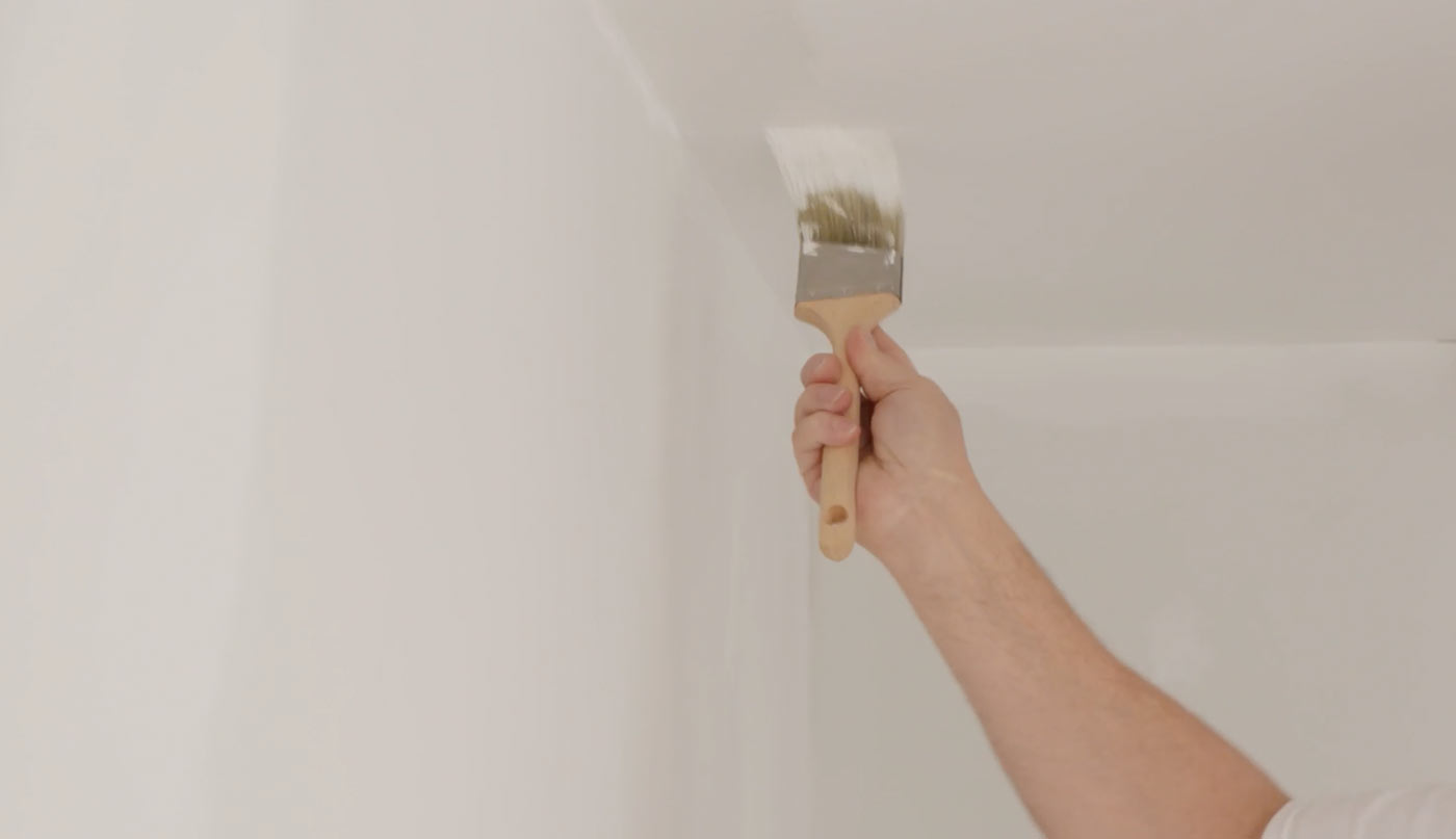 Homme recouvrant le plafond de peinture blanche.