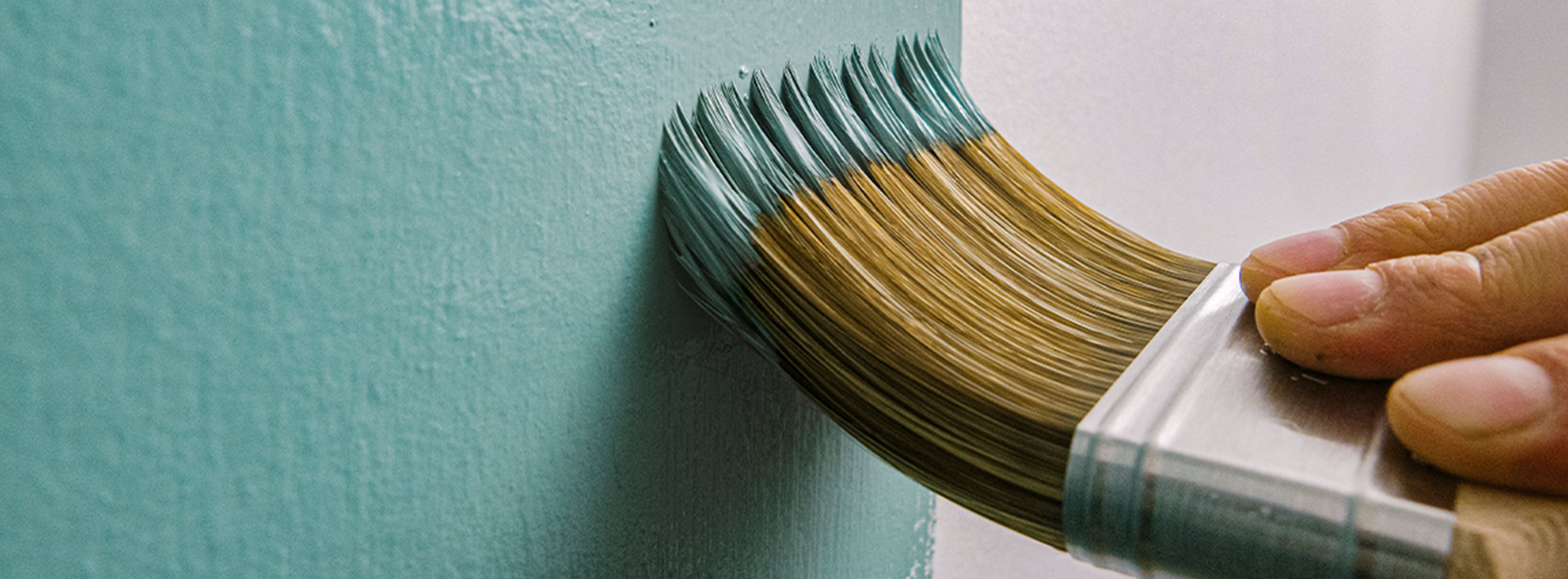 A homeowner using a brush to paint a wall teal.
