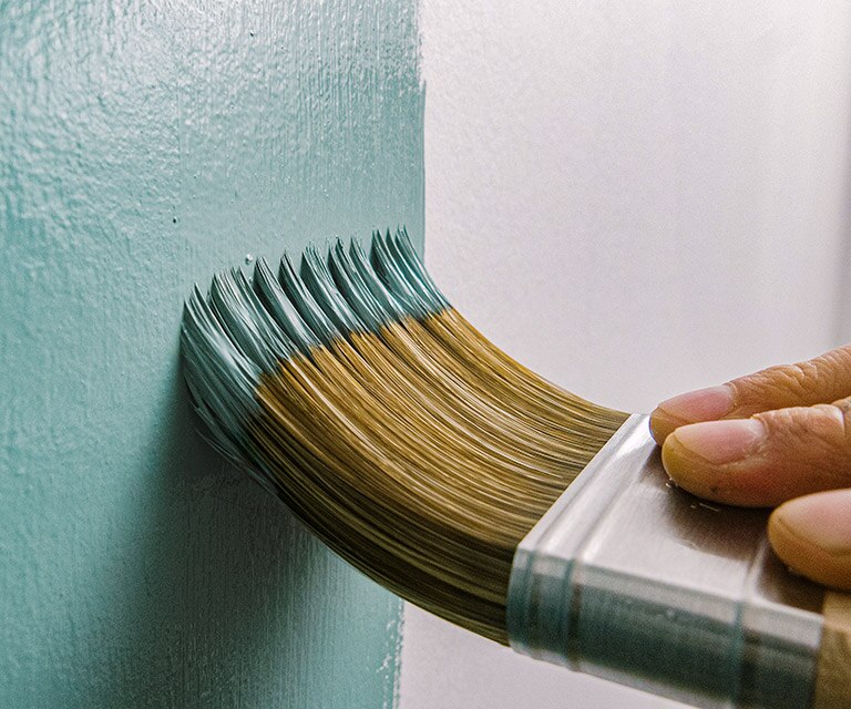 A homeowner using a brush to paint a wall teal.