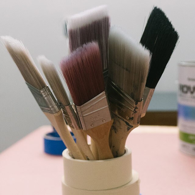 A variety of paintbrushes clustered together inside stacked rolls of tape.