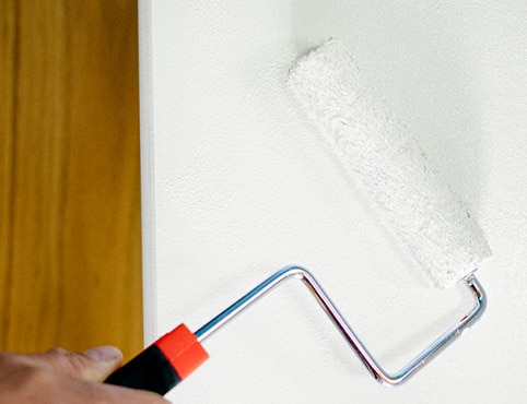 A close up of a roller painting a white wall.