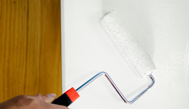 A close up of a roller painting a white wall.