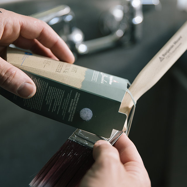 A person places a paintbrush back into its original packaging to maintain bristle shape.