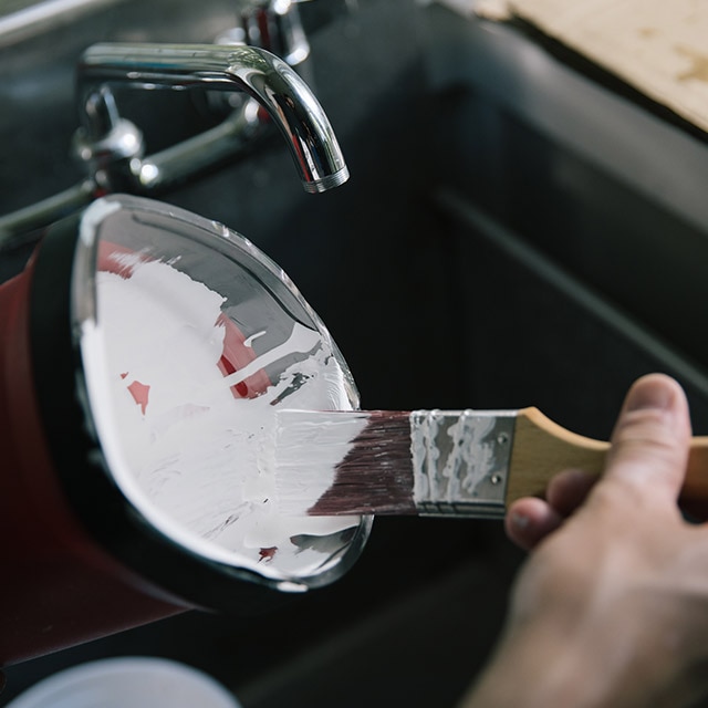 Removing excess paint from the brush by pressing it against the inside lip of the paint can.