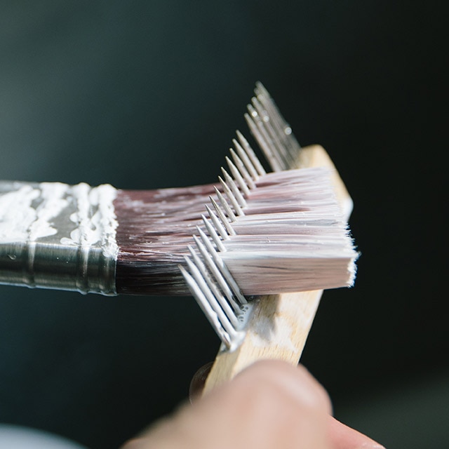 A person removes excess water from a paintbrush by using a brush comb.