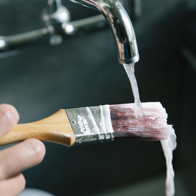 Rinsing paintbrush under running water. 