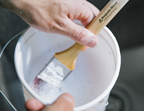 A close-up of soaking paintbrush in a bucket of soapy water.