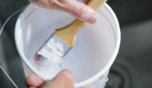 A close up of soaking paintbrush in a bucket of soapy water.