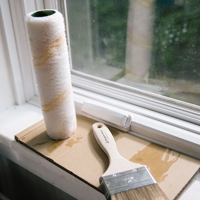 A clean roller cover and paintbrush sitting on a windowsill.
