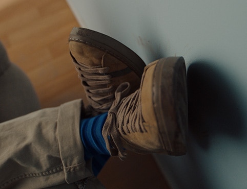 A person reclining on a couch rests his shoed feet against a light green-painted wall. A person reclining on a couch rests his shoed feet against a light green-painted wall.