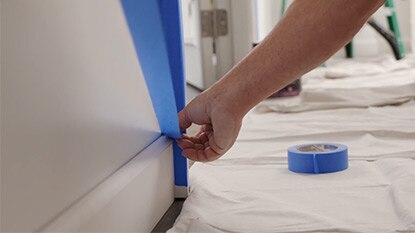 Painting contractor applying tape in preparation to cutting paint in a room