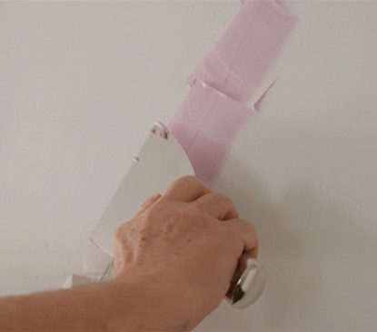 Homeowner uses a putty knife to fill a ceiling crack. 