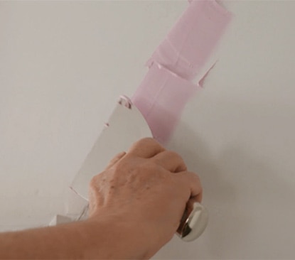 Homeowner uses a putty knife to fill a ceiling crack.