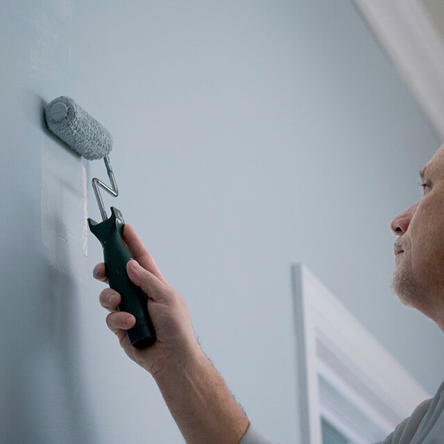A homeowner uses a paint roller to apply paint to a wall.