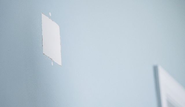 Mur bleu présentant une surface carrée de réparation d’un trou.