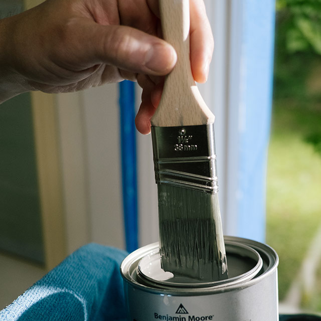 A homeowner dips a paintbrush into a quart of ADVANCE interior paint in satin finish.