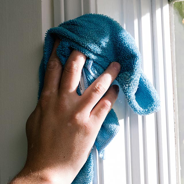 A homeowner cleans their window trim.