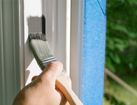 A homeowner painting white window trim with gray paint.