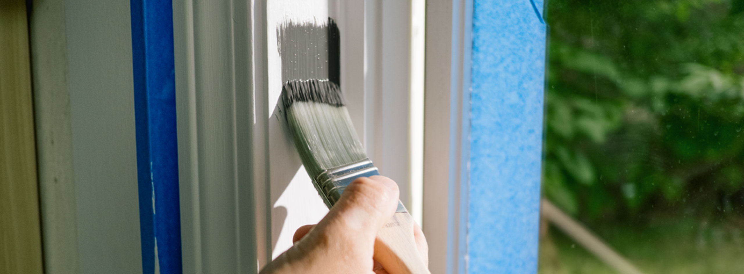 Un propriétaire peint une moulure de fenêtre blanche avec de la peinture grise.