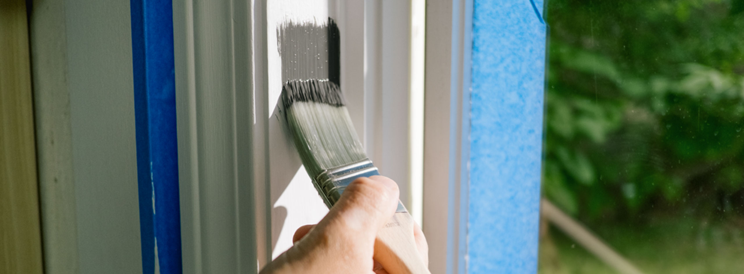 A homeowner painting white window trim with gray paint.