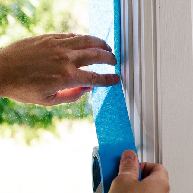 A homeowner applies painter's tape to a windowpane.