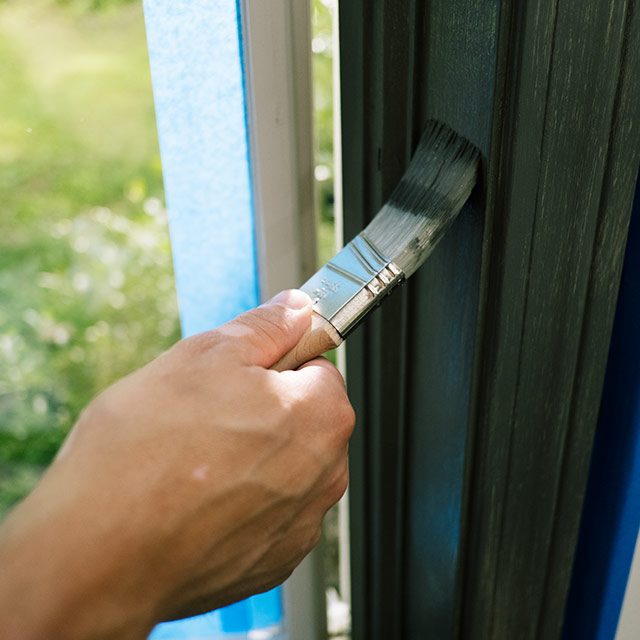 Un dueño de casa aplicando una capa adicional de pintura sobre un marco de ventana. Un dueño de casa aplicando una capa adicional de pintura sobre un marco de ventana.