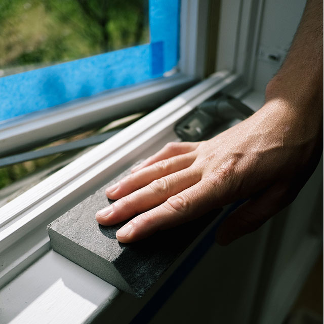 A homeowner sanding their window trim.