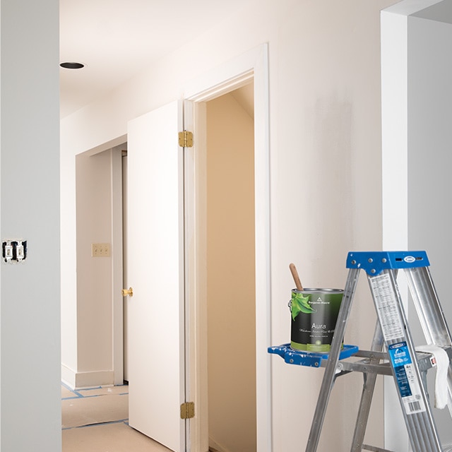 Open can of Benjamin Moore® Aura® white interior paint in a resting on a ladder. Open can of Benjamin Moore® Aura® white interior paint in a resting on a ladder.