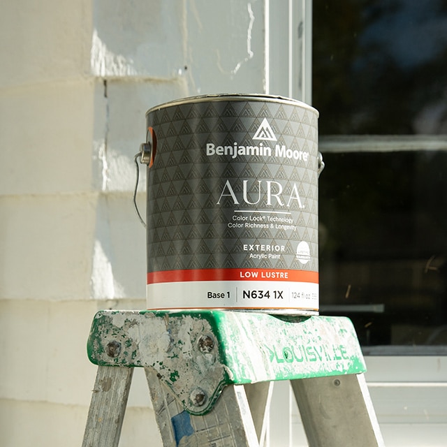 An open gallon of Benjamin Moore AURA® Exterior paint resting on a ladder.