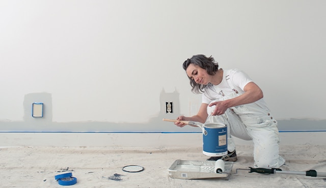 A woman holding a 3.79 L can of paint preparing to paint a wall.