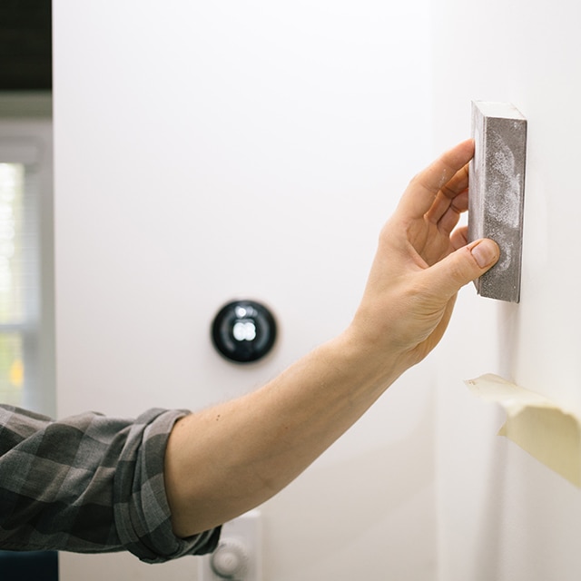 A homeowner sanding a white wall/