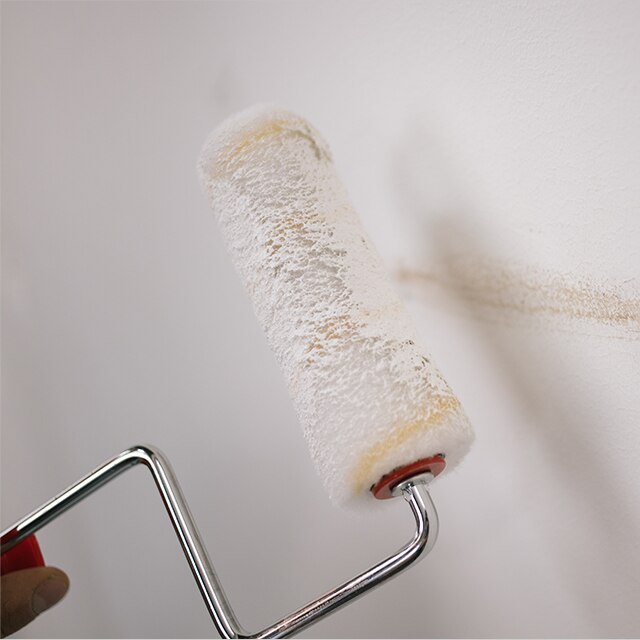 A homeowner painting over a scuff on a white wall using a paint roller.
