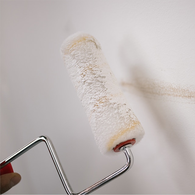 Un dueño de casa pinta con un rodillo una rozadura en una pared blanca. Un dueño de casa pinta con un rodillo una rozadura en una pared blanca.