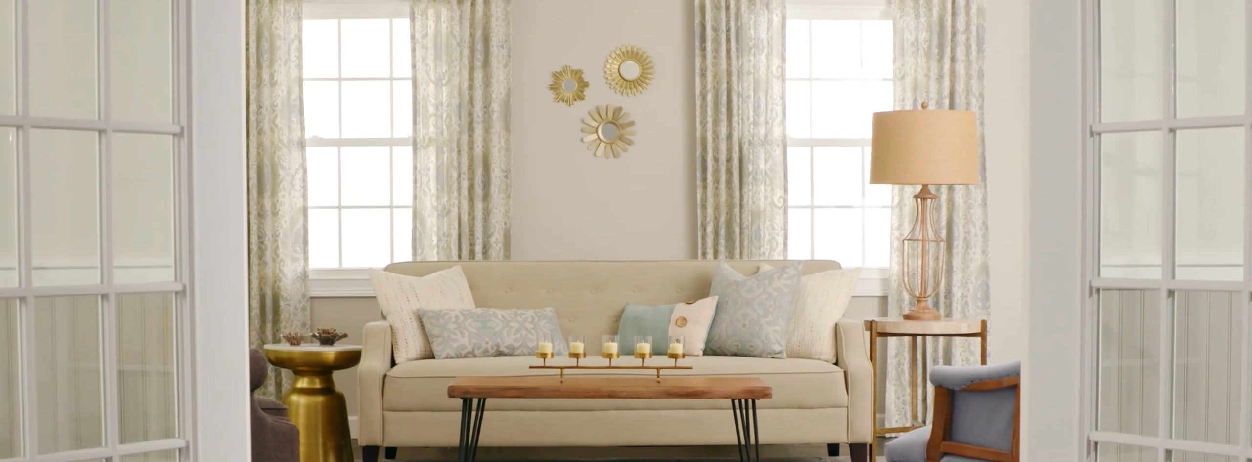 Un salon à la décoration neutre avec un mur blanc cassé, des moulures blanches et des portes-fenêtres.