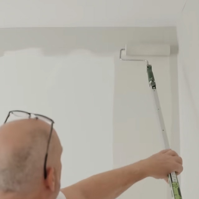 Un homme applique au rouleau de la peinture blanc cassé sur un mur.