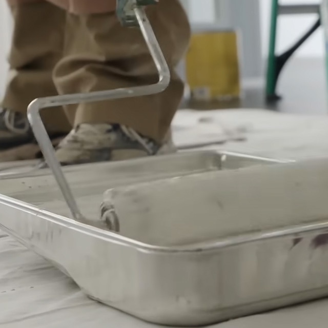 Gros plan d’une personne qui retrempe son rouleau dans un bac rempli de peinture blanche.