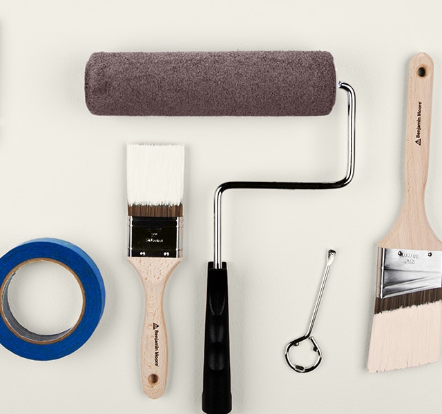 A collection of painting supplies, including paintbrushes, a paint roller, painter’s tape, a paint tray containing brown paint, and more.