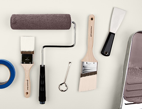 Una colección de suministros de pintura, incluidos pinceles, un rodillo, cinta de pintor, una cubeta de pintura con pintura de color marrón y más.