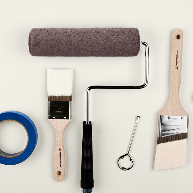 A collection of painting supplies, including paintbrushes, a paint roller, painter’s tape, a paint tray containing brown paint, and more.