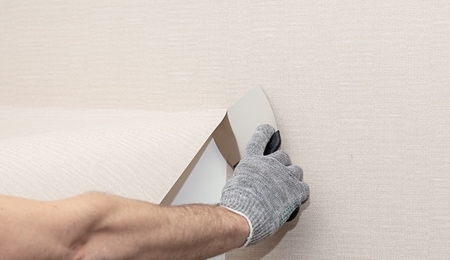 A homeowner removing wallpaper from a white wall.