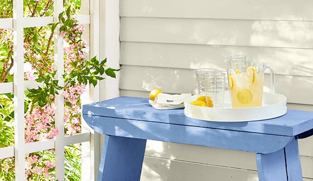 Off-white exterior siding with a blue bench holding a pitcher of lemonade.