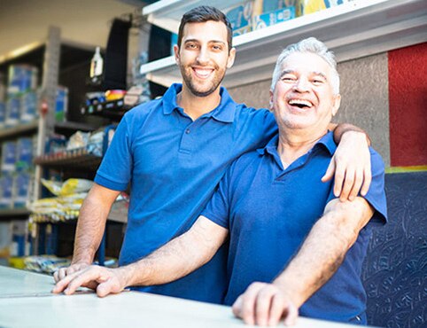 A father-and-son retailer team behind the counter in their Benjamin Moore store; the son has his arm around the father’s shoulders, and they are both smiling. A father-and-son retailer team behind the counter in their Benjamin Moore store; the son has his arm around the father’s shoulders, and they are both smiling.