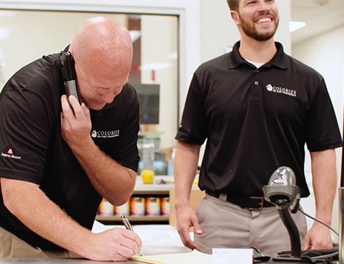Deux détaillants Benjamin Moore portant une chemise noire se tiennent derrière un comptoir. L’un d’eux parle au téléphone et prend des notes.