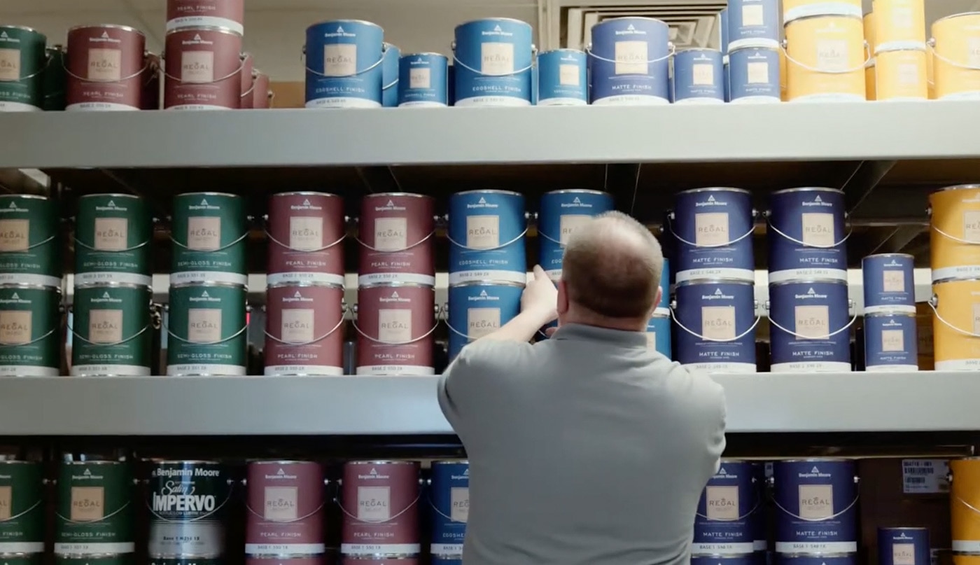 A man wearing a gray shirt standing in front of a wall with rows of Regal® Select Interior paint cans.