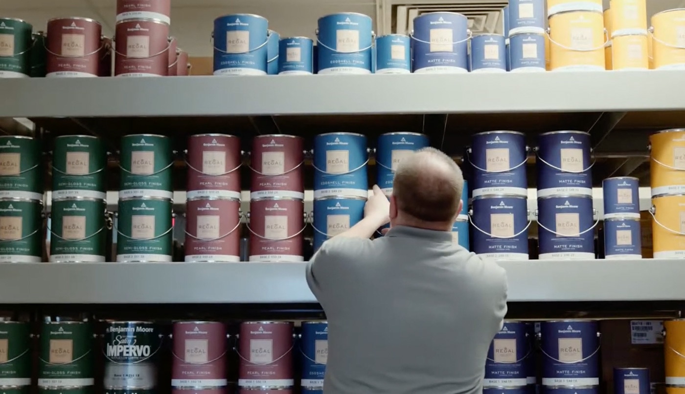 A man wearing a gray shirt standing in front of a wall with rows of REGAL® Select Interior paint cans.