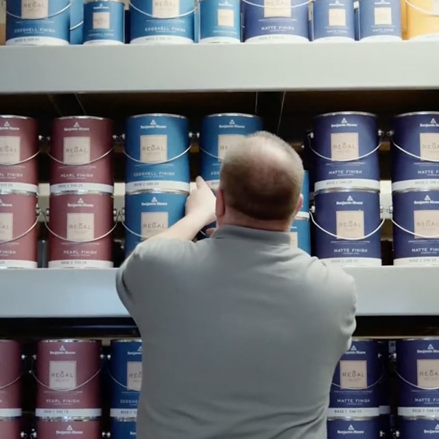 A man wearing a gray shirt standing in front of a wall with rows of REGAL® Select Interior paint cans.