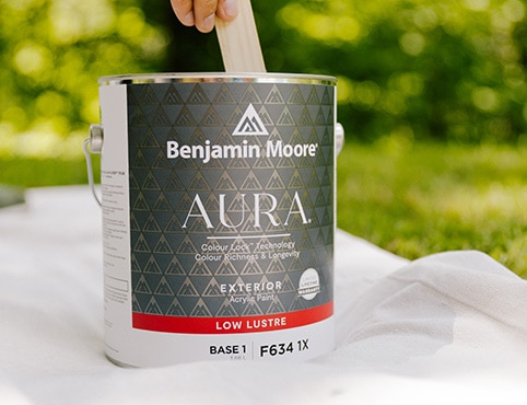 A person stirring an open can of AURA Exterior paint.