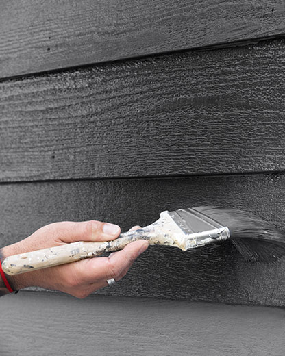 A person applying black AURA® Exterior paint on siding using a paintbrush.