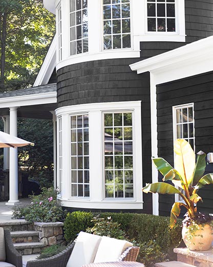 A house painted with black AURA® Exterior paint, with white trim and pillar, and outdoor furniture.